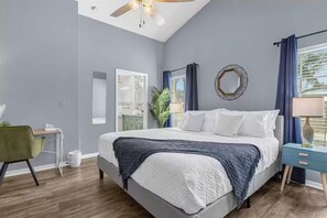 Ein Schlafzimmer mit einem Bett, einem Schreibtisch, einem Stuhl, einem Spiegel und einem Fenster mit Vorhängen.
