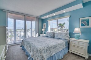 A bedroom with a large bed, a nightstand, a dresser, and a view through a sliding glass door. - Beach Front Bliss at Anna Maria Island Club 40 (Bradenton Beach)