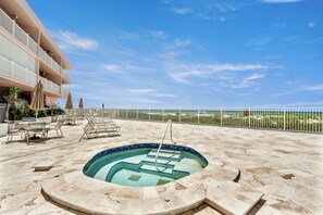 En pool på taket med fri utsikt över havet, omgiven av solstolar och en byggnad med balkonger.