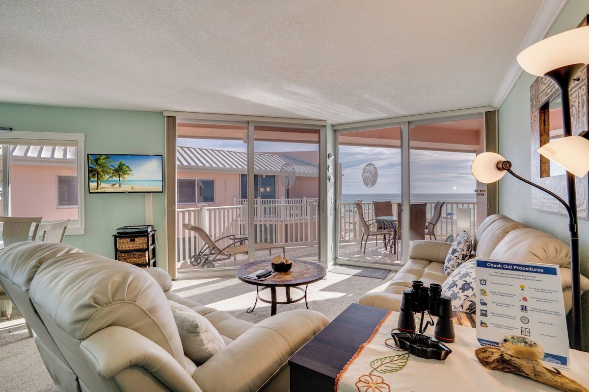 A room with a balcony, a sofa, a table with binoculars, and a sign about check-out procedures.