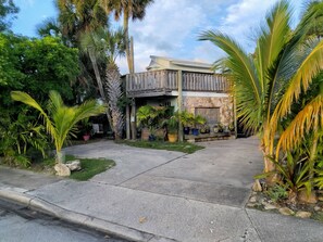 Una casa a due piani con facciata in pietra, un balcone e un giardino antistante con diverse piante.