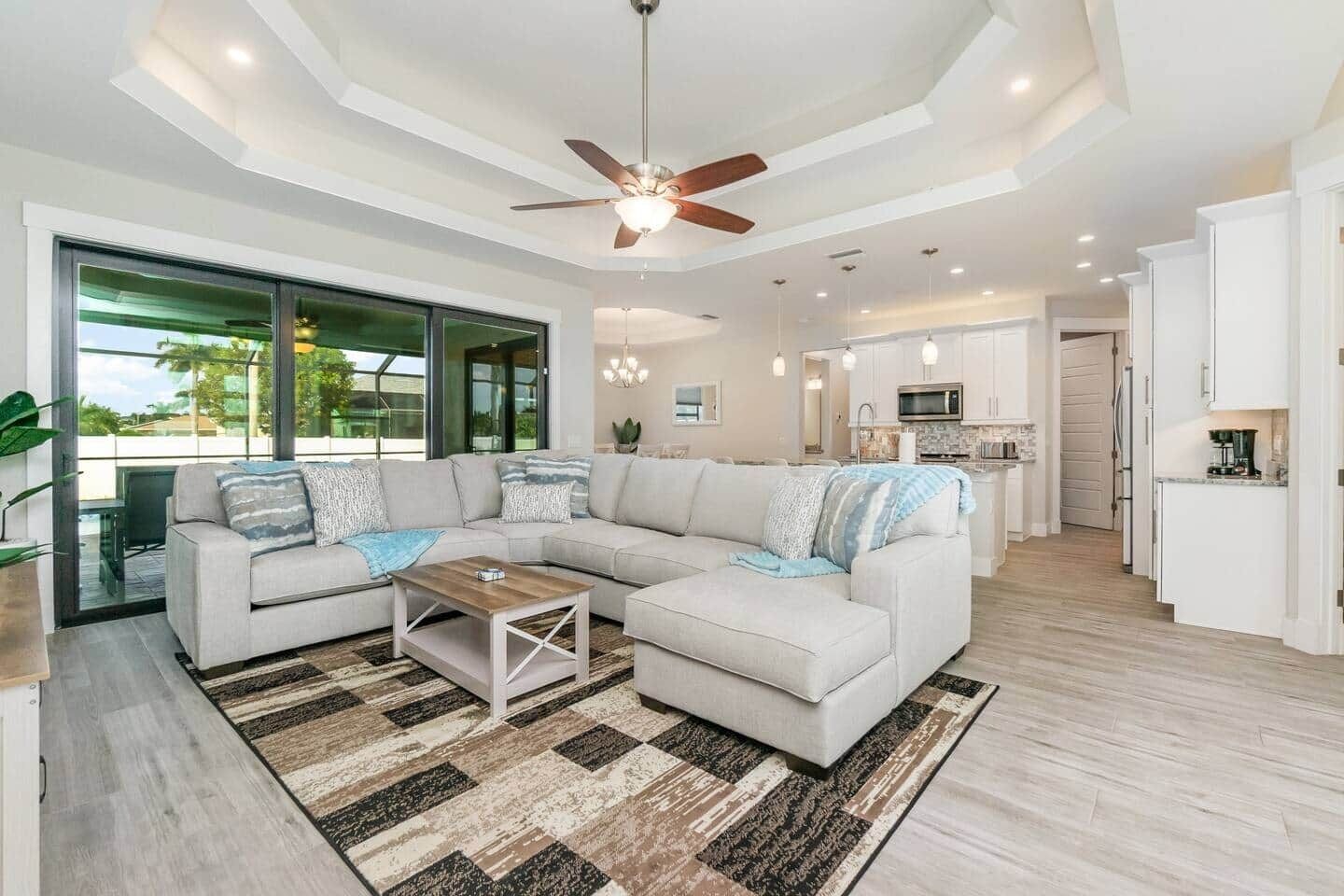 A modern living room with a sectional sofa, a coffee table, and a view of the kitchen and dining area.