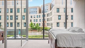 Quarto de hotel moderno com uma janela grande, uma cama e vista para a fachada do edifício.