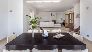 A modern dining area with a dark wooden table, white chairs, a vase with a plant, and a bottle of champagne. - Blue Heaven Luxury V5 (Porches)