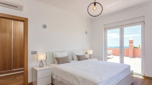 A bedroom with a large bed, two bedside tables, a wooden wardrobe, and a view of the outside. - Blue Heaven Luxury V5 (Porches)