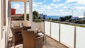 A balcony with wicker furniture, a table with glasses and a bottle, and a view of the sea and buildings. - Luxury Vau Beach Villa with Private Heated* Pool (Portimão)