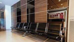 Une salle d’attente avec une rangée de chaises noires et un mur en bois sur lequel est affiché un panneau indiquant « DECO ».