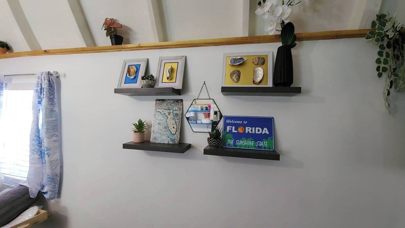 Un mur doté de plusieurs étagères où sont exposés divers objets, notamment des photos encadrées, une pancarte d’accueil de l’État de Floride et des objets décoratifs.