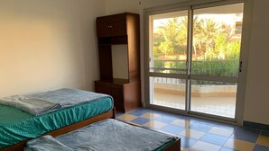 A room with two beds, a wardrobe, and a sliding glass door leading to an outdoor area.