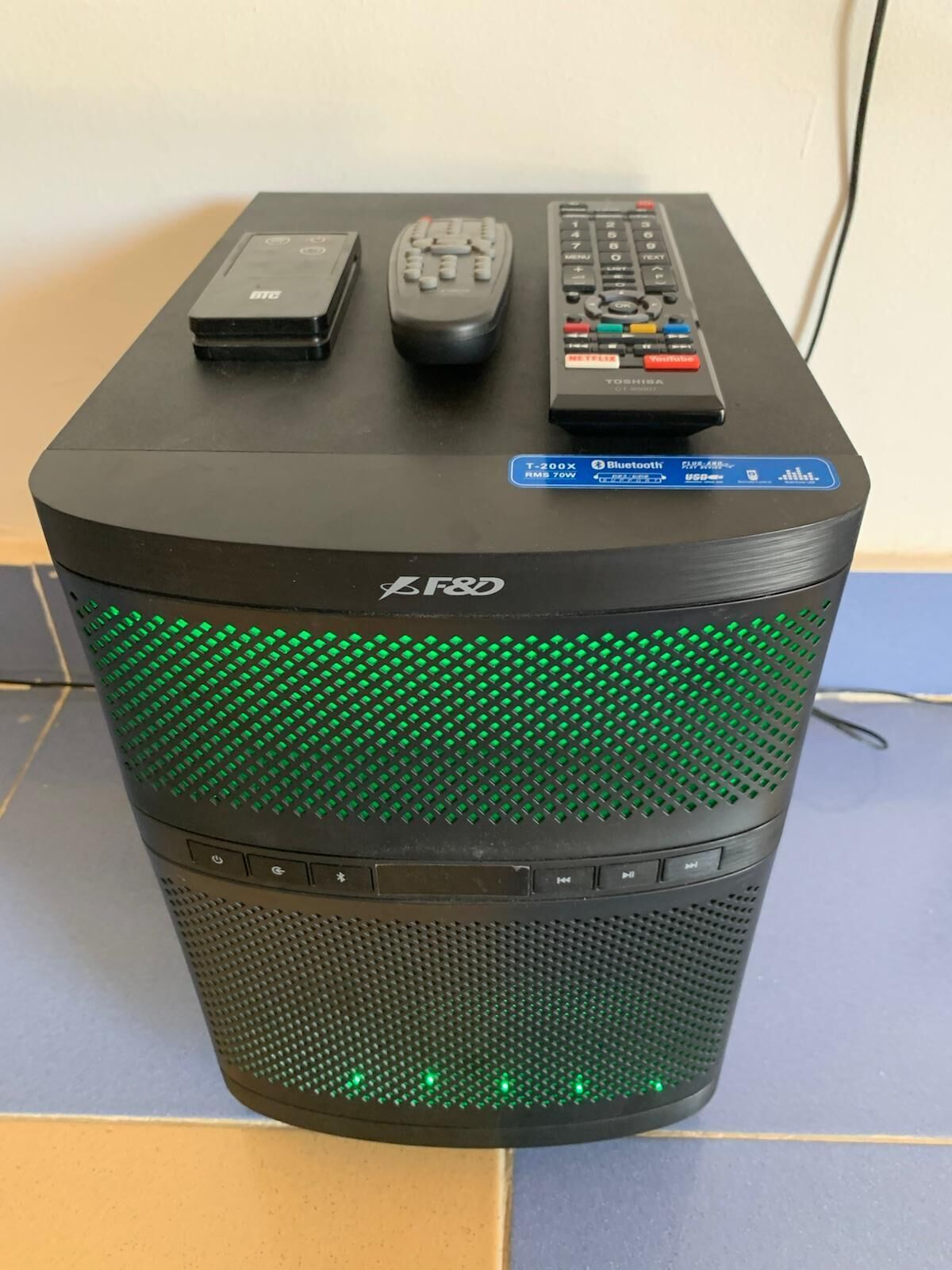 A black F&D speaker with green LED lights, a T-200X router, and two remote controls on top.