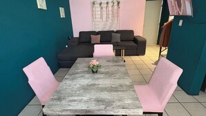 A living room with teal walls, a dark sofa set, a wooden coffee table with a pink cushion, and a pink chair.