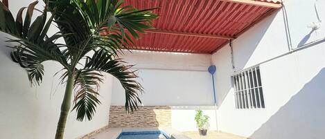 Una piscina con bordes de azulejos, una palmera y una zona con techo rojo.