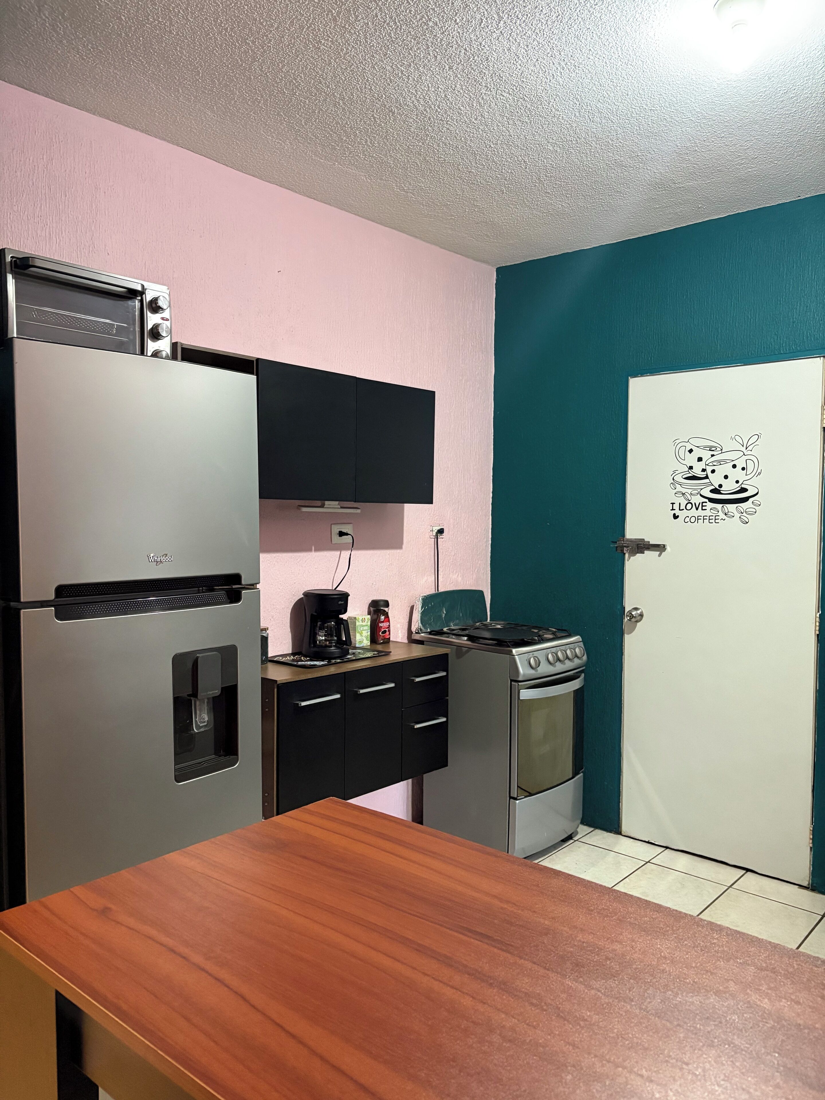 Cocina compacta con refrigerador, estufa y microondas. Hay una cafetera en la encimera y un adhesivo en la puerta.