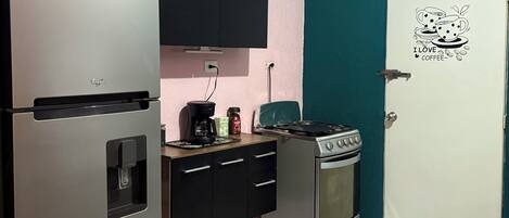 Cocina compacta con refrigerador, estufa y microondas. Hay una cafetera en la encimera y un adhesivo en la puerta.