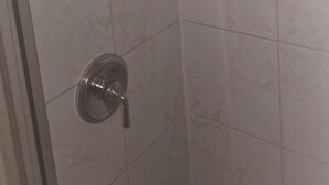 Una doccia con soffione a mano e una bottiglia di shampoo su uno scaffale.