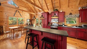 A spacious kitchen with wooden beams, red cabinets, and a large island with stools. - Log Cabin Near Skiing–Sugars Cozy Cabin (Sugar Mountain)