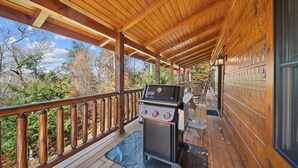 A covered wooden deck with a grill and outdoor seating. - Log Cabin Near Skiing–Sugars Cozy Cabin (Sugar Mountain)