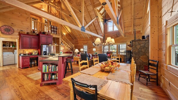 A spacious wooden interior with a dining area, kitchen, and a stone fireplace. - Log Cabin Near Skiing–Sugars Cozy Cabin (Sugar Mountain)
