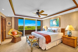 A spacious bedroom with a large bed, a ceiling fan, a view of a lush landscape through a sliding glass door, and a wicker chair. - Maui Kaanapali | Penthouse 2 BR | Car Incl. w/ 6+ Nights | MKV-A606 by KBM (Lahaina)