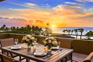 Ein Esstisch für zwei Personen mit Sonnenuntergangsblick, zwei Blumenvasen und einer Kerze auf einem Balkon mit Meerblick.