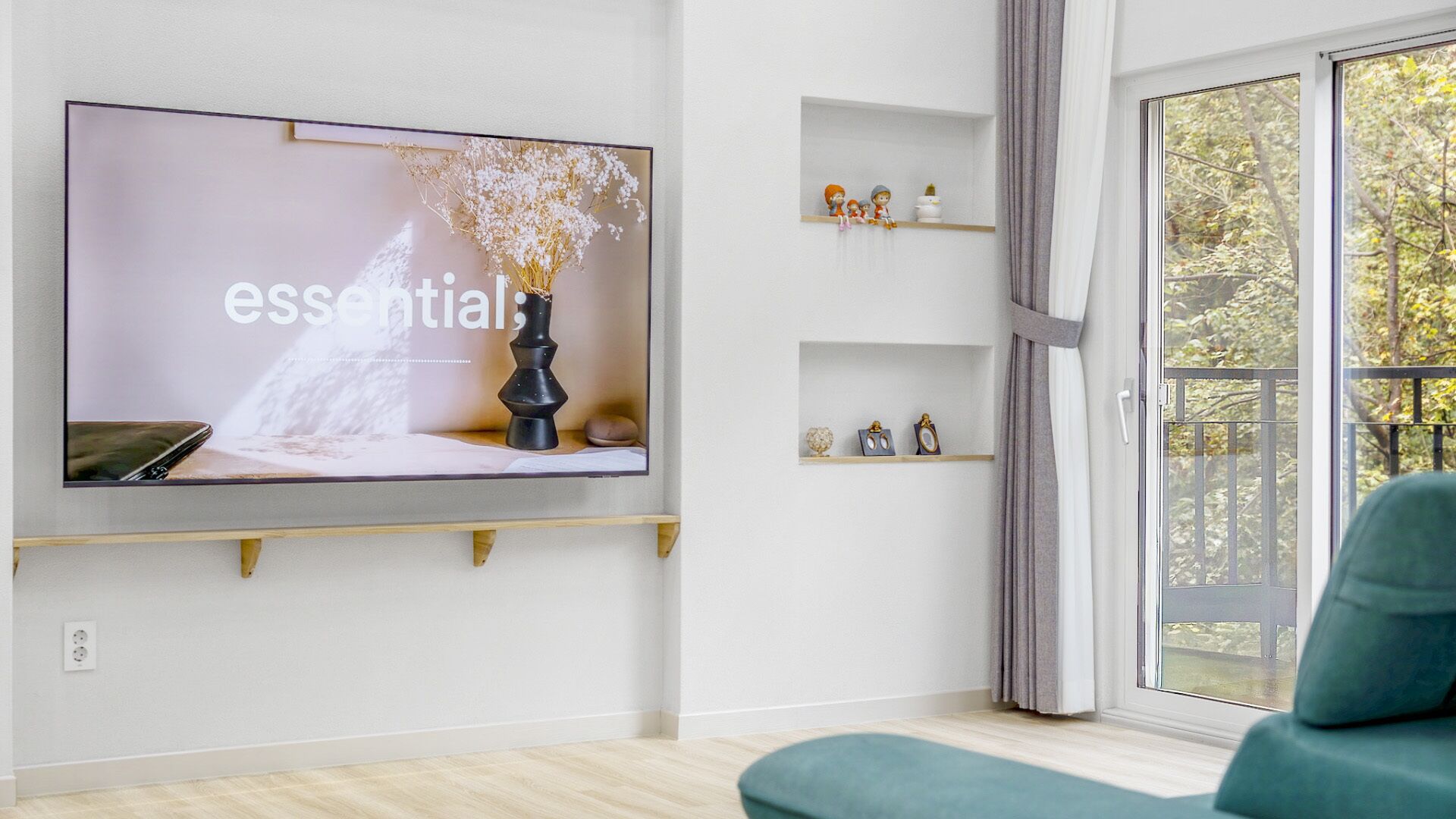 A modern living room with a large flat-screen TV mounted on the wall, a sofa, and a window with a view of trees.