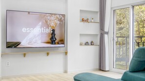 Ett modernt vardagsrum med en stor platt-TV som är monterad på väggen, en soffa och ett fönster med utsikt över träd.