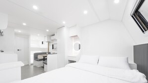 A modern, white-themed bedroom with a large bed, a seating area, and a built-in desk. - Gangneung Pinehill Park Pension&caravan (Gangneung)