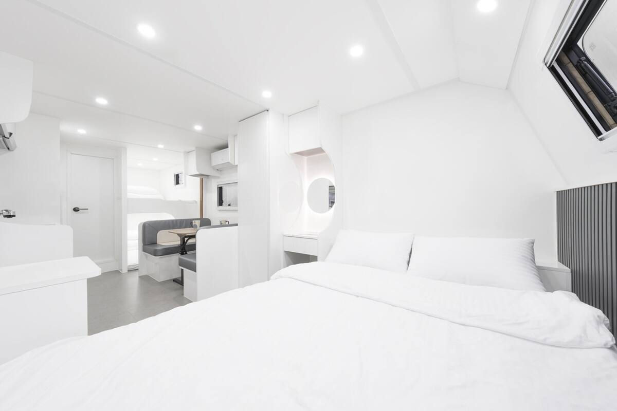 Ein modernes Schlafzimmer in Weiß mit einem großen Bett, einer Sitzecke und einem integrierten Schreibtisch.