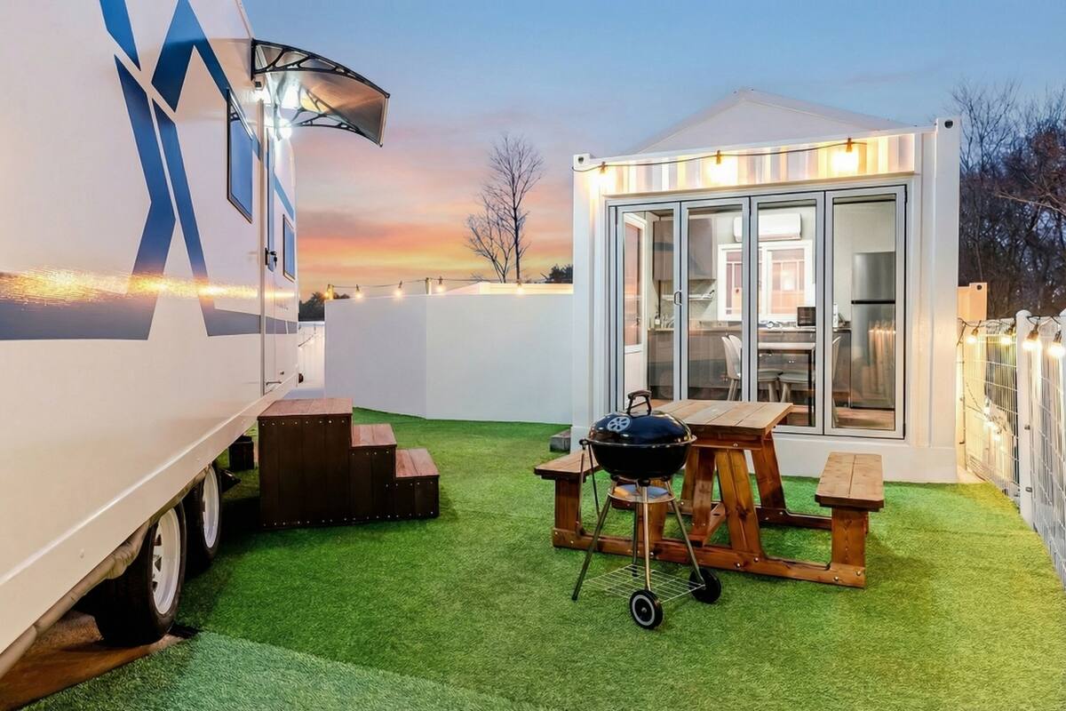 Ein Wohnmobil mit einer Terrasse, die einen Grill, Holztische und eine Küchenzeile mit Glasfronten bietet.