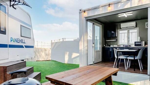 A RV with "Pinehill" branding, a wooden picnic table, and a kitchen area with a dining set. - Gangneung Pinehill Park Pension&caravan (Gangneung)