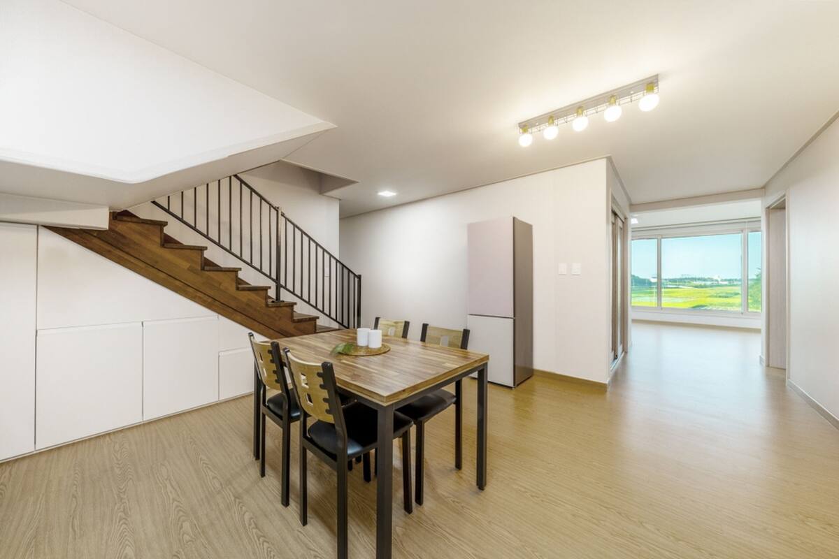 Un interior moderno con zona de comedor, escalera y grandes ventanales que ofrecen vistas al exterior.