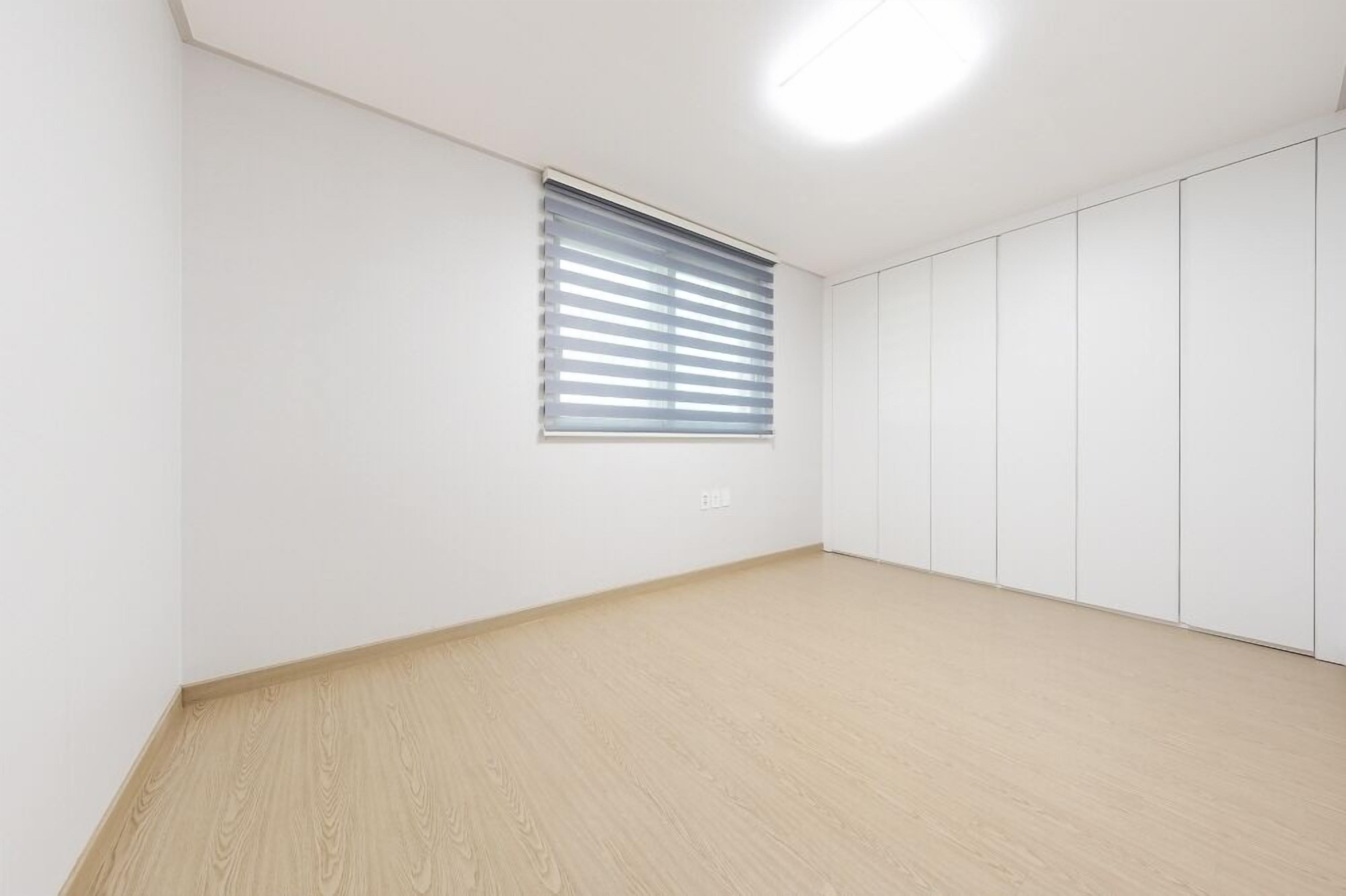 A room with a large window, white walls, and a wooden floor.