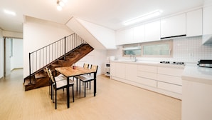 Una cocina moderna con armarios blancos, una mesa de comedor de madera y una escalera con barandillas negras.
