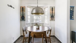 A dining area with a round table, four chairs, a hanging pendant light, and artwork on the walls.