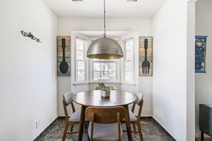 Un comedor con una mesa redonda, cuatro sillas, una lámpara colgante y obras de arte en las paredes.
