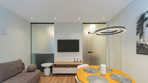Una sala moderna con un sofá, una mesa redonda de comedor con individuales, un televisor montado en la pared y una lámpara contemporánea.