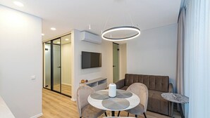 Ein modernes Wohnzimmer mit einer Couch, einem Esstisch und einem an der Wand befestigten Fernseher.