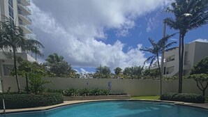 Una piscina con borde de ladrillo, rodeada de palmeras y un muro bajo.