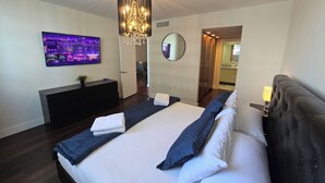 Una habitación de hotel moderna con una cama grande, un televisor montado en la pared, una araña y un espejo.