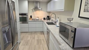 Una cocina moderna con electrodomésticos de acero inoxidable, encimera de mármol y un lavamanos.
