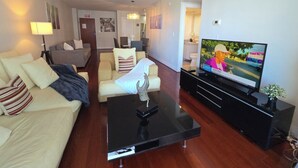 Una sala moderna con un televisor de pantalla plana, una mesa de centro de cristal y un sofá.