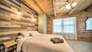 Une chambre avec un mur recouvert de lambris en bois, un lit avec une couette blanche, une table de chevet et un ventilateur de plafond.