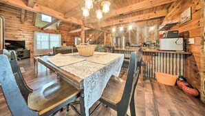 L’intérieur d’un chalet rustique en bois comprend une table à manger, des chaises, une cheminée et un coin cuisine.