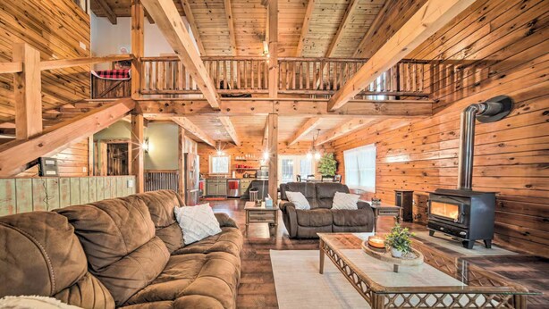 L’intérieur d’un chalet confortable, avec des murs en bois, un escalier en bois, une cheminée et un espace de vie comprenant des canapés et une table basse.
