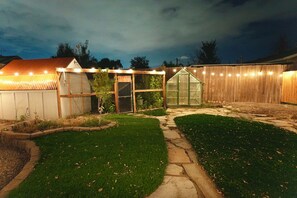 Un jardin avec une pergola en bois, une serre et un chemin en pierre.