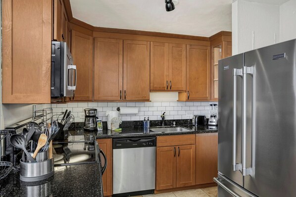A modern kitchen with wooden cabinets, stainless steel appliances, and a dishwasher. - Kaanapali Shores | Ocean View 4 BR, Sleeps 12 | Car Incl. w/ 6+ Nights | KS ML-2481 by KBM (Lahaina)