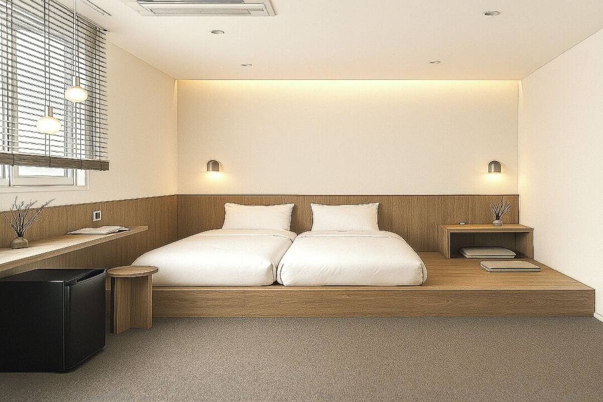 A modern hotel room with a double bed, bedside tables, a small desk, and a window with blinds.