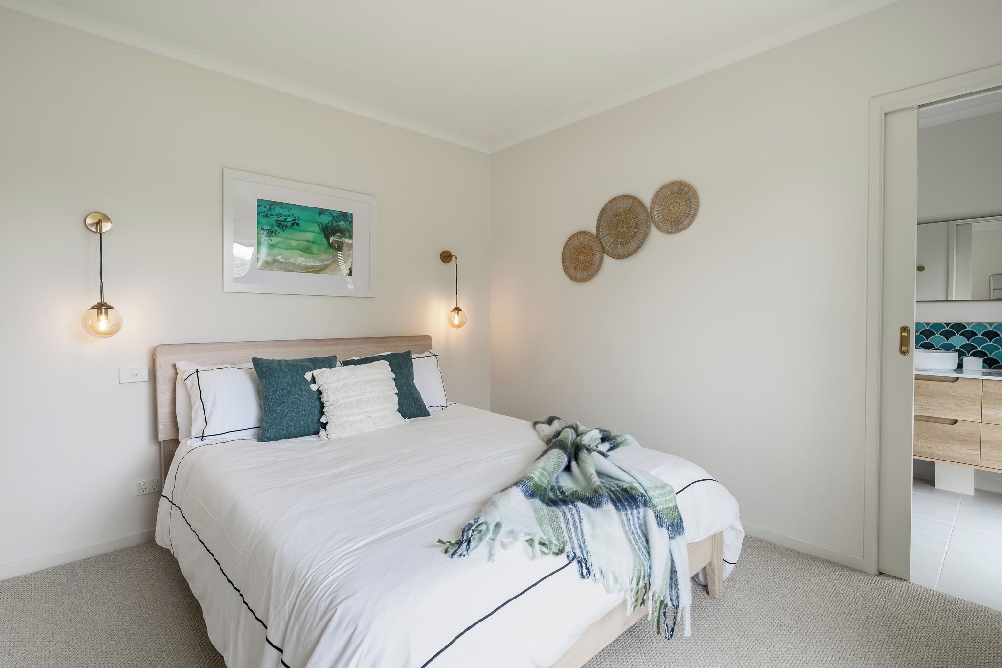 A neatly arranged bedroom with a bed, bedside lamps, a framed picture, and decorative wall art.