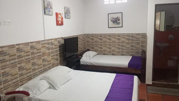 A room with two beds, a TV, and a bathroom with a mirror and sink. - HOTEL CASA JAIRO (Neiva)