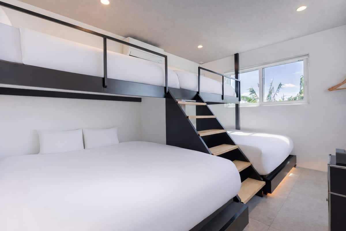 Una habitación de hotel moderna con literas, una escalera, un ventanal con vistas y un pequeño escritorio.